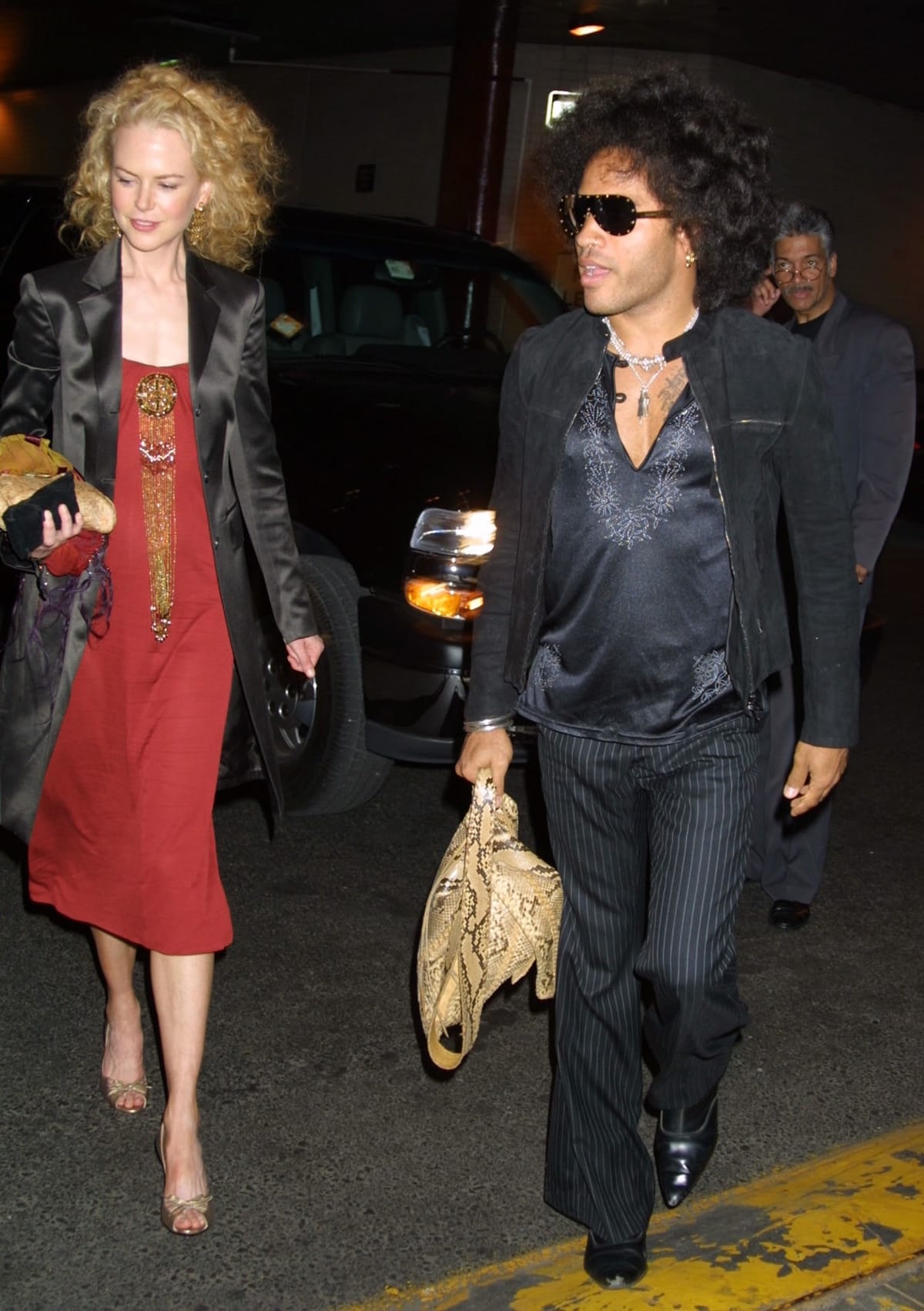 Nicole Kidman and Lenny Kravitz step out for a stylish early-2000s date night—Kidman in a red slip dress, satin coat, and metallic peep-toe heels, and Kravitz in pinstriped trousers, a silk shirt, and pointed black boots