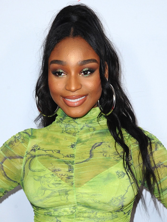 Normani wearing a curled half-up ponytail and green smoky eye makeup