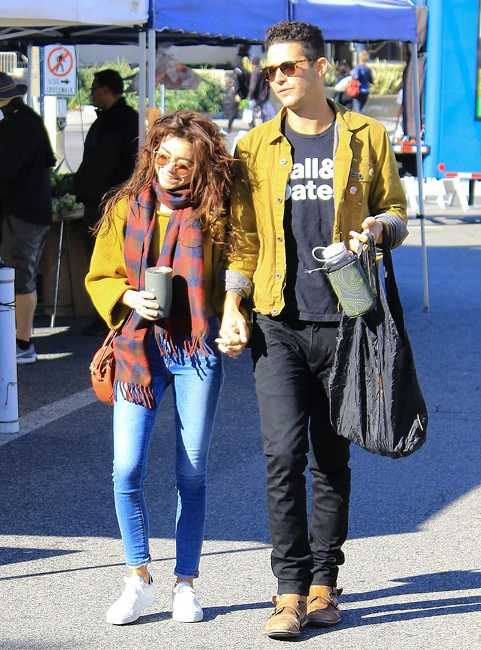 Sarah Hyland wearing white sneakers with jeans and a mustard sweater beside Wells Adams at a Los Angeles farmers market