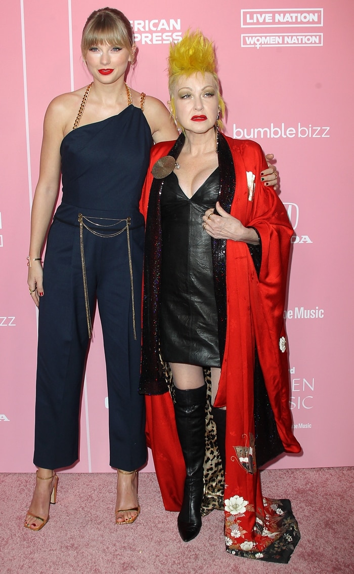 Taylor Swift stuns in a navy Oscar de la Renta jumpsuit with chain accents and gold Sergio Rossi SR1 sandals, while Cyndi Lauper rocks an edgy black leather dress, thigh-high boots, and a bold red kimono for a punk-glam statement