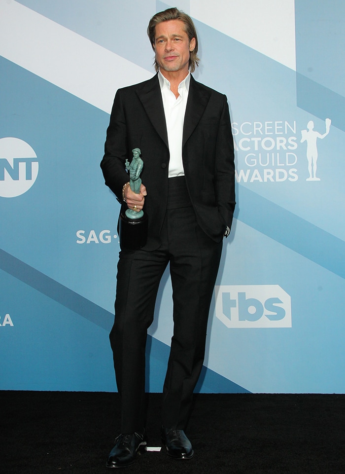 Brad Pitt accepts Outstanding Performance by a Male Actor in a Supporting Role at the 26th SAG Awards on January 19, 2020, wearing a custom black Brioni tuxedo styled with polished black leather dress shoes, a relaxed open-collar “air tie,” and a classic cummerbund—an effortless twist on traditional awards-season tailoring