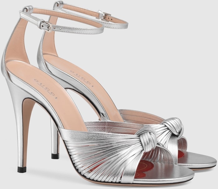 Gucci’s silver metallic leather sandals feature knotted multi-strap detailing, open toes, slim ankle straps, and high stiletto heels
