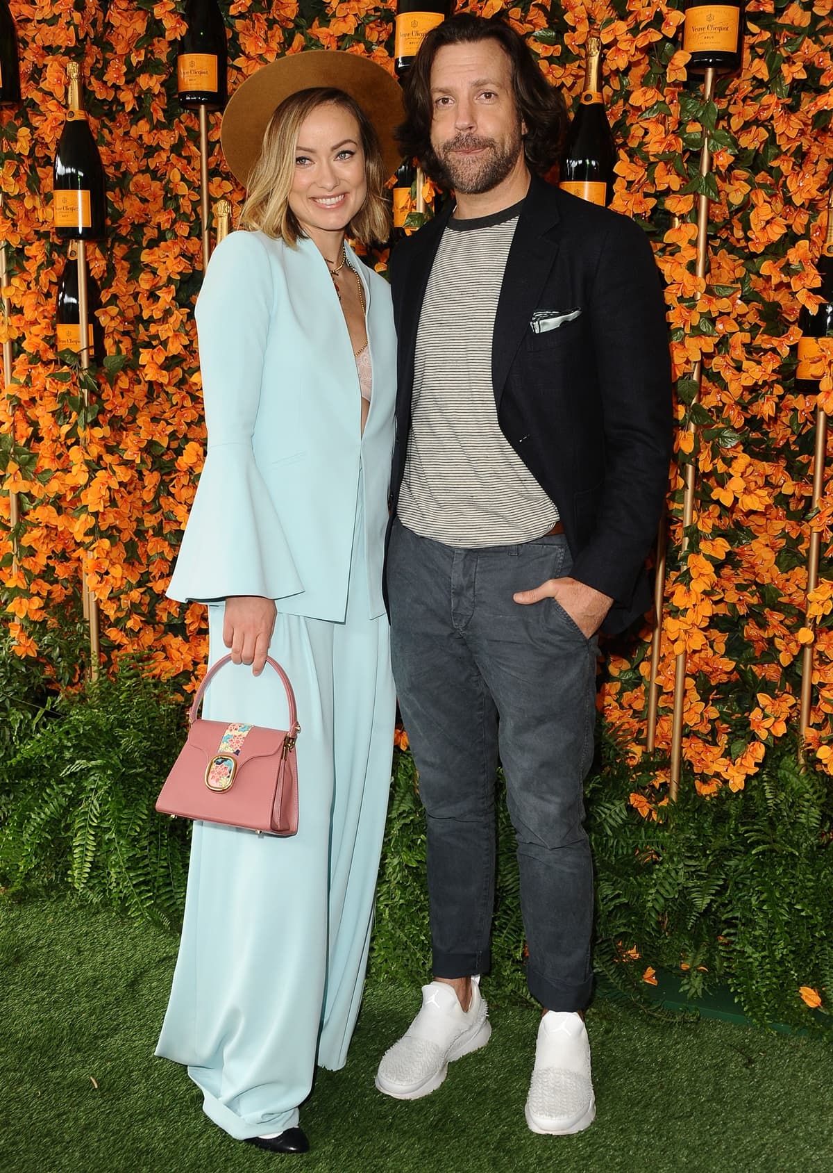 Olivia Wilde, wearing a fluid Alice + Olivia suit styled with classic black ballet flats, a Lidia May Pema top-handle bag, and Foundrae jewelry, arrives alongside Jason Sudeikis at the 9th Annual Veuve Clicquot Polo Classic Los Angeles at Will Rogers State Historic Park on October 6, 2018, in Pacific Palisades, California