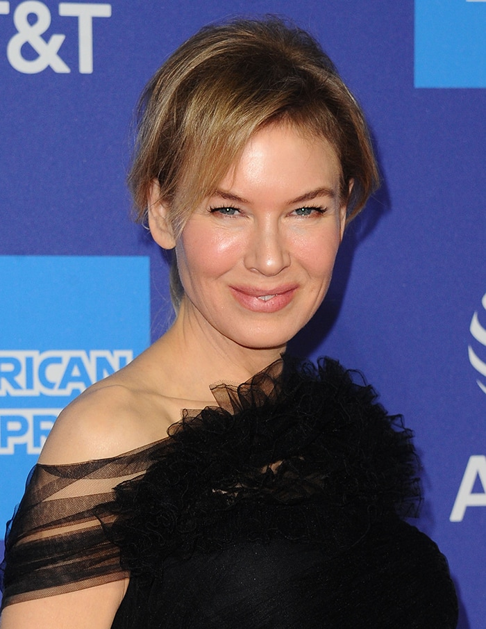 Wearing her hair swept back with soft, face-framing strands, Renée Zellweger lets the asymmetrical neckline and delicate tulle accents take center stage