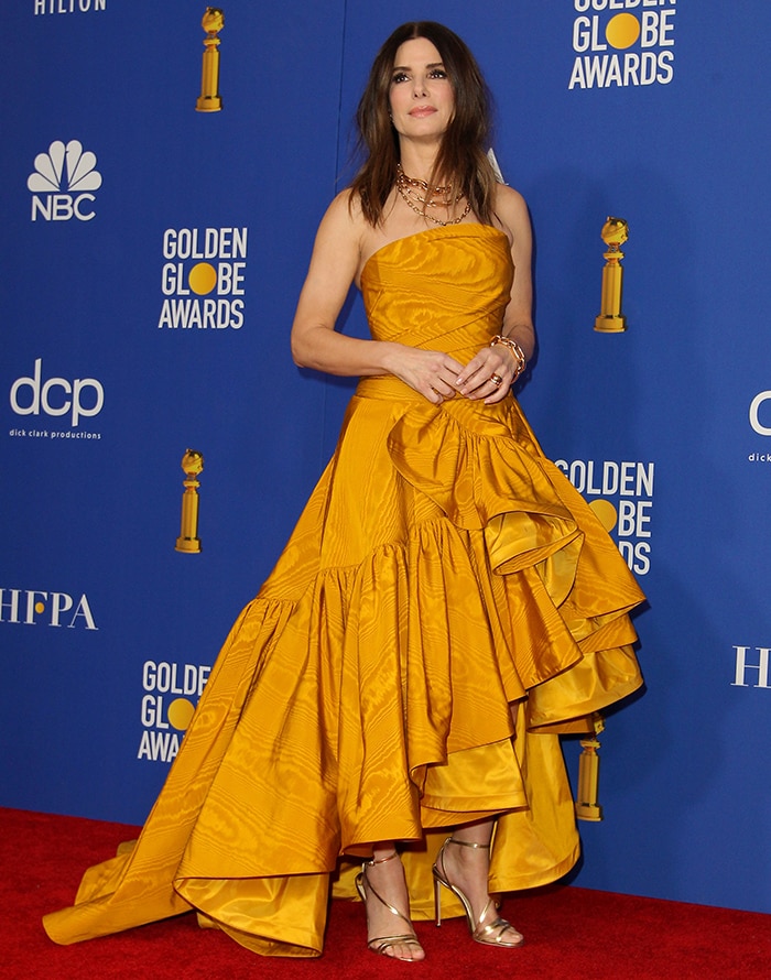 Sandra Bullock commands the stage at the 2020 Golden Globe Awards in a marigold-yellow Oscar de la Renta high-low gown, revealing metallic Jimmy Choo Tesca sandals that add a sleek, red-carpet finish beneath the sculptural hem