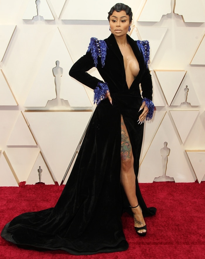 Blac Chyna paired her dramatic velvet Oscar gown with black ankle-strap platform sandals, revealing a thigh-high slit and colorful leg tattoos on the Hollywood red carpet