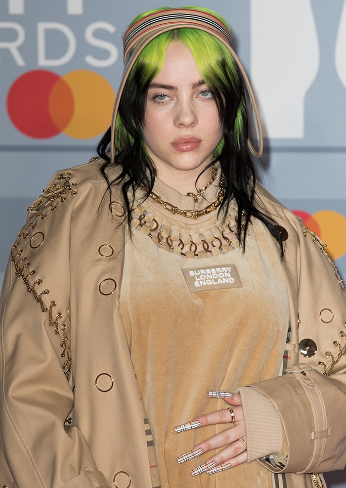 Billie Eilish finishes the look with Burberry check accents—from her visor to her graphic socks and long plaid nails—tying the heritage motif into her signature green-and-black hair