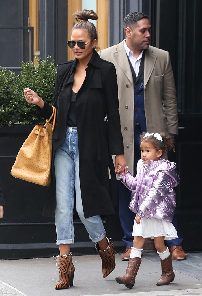 Chrissy Teigen steps out in New York City with daughter Luna on February 20, 2020, elevating cuffed jeans and a black coat with Saint Laurent's zebra-print 'Niki' ankle boots, while carrying a striking ostrich Hermès Birkin bag