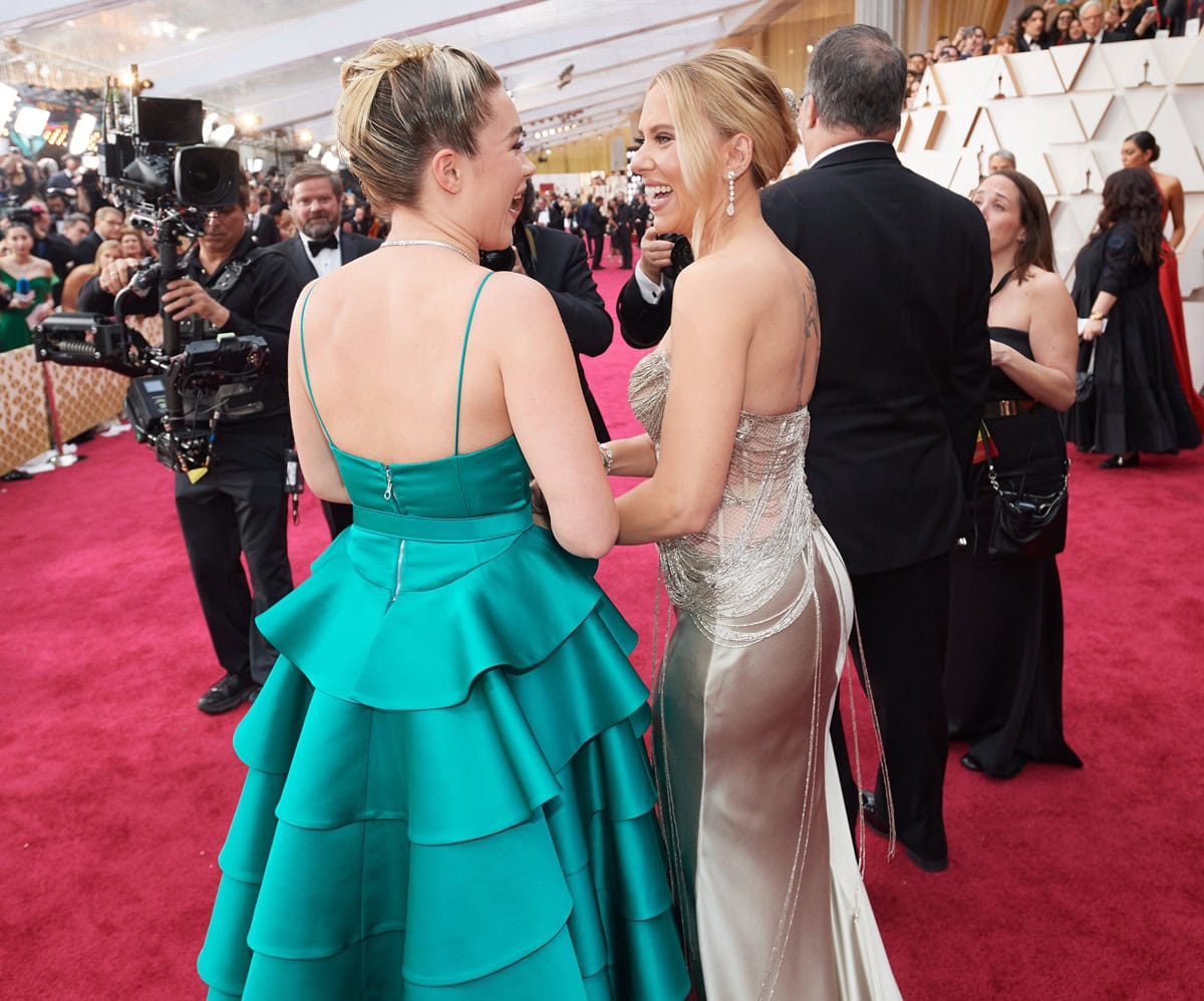 Florence Pugh shares a laugh with fellow Oscar nominee Scarlett Johansson on the red carpet at the 92nd Academy Awards, showcasing the dramatic tiered back of her custom teal Louis Vuitton gown
