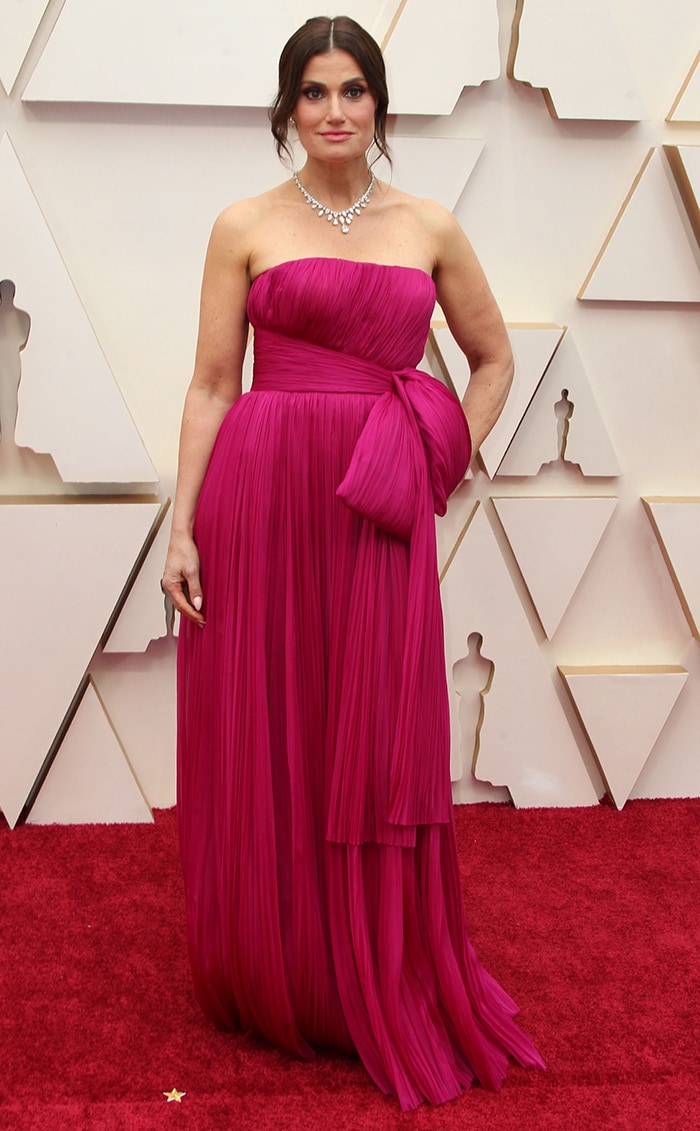 Idina Menzel wore a strapless magenta J. Mendel gown featuring finely pleated silk, a sculptural waist bow, and a flowing layered skirt that moved elegantly with each step