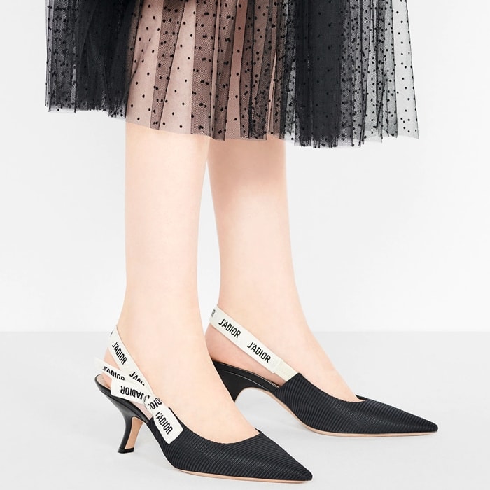 Dior’s black technical fabric J’Adior slingbacks combine a sculpted pointed toe with the house’s signature embroidered ribbon straps, creating a sleek logo-driven pump that became a defining late-2010s luxury staple