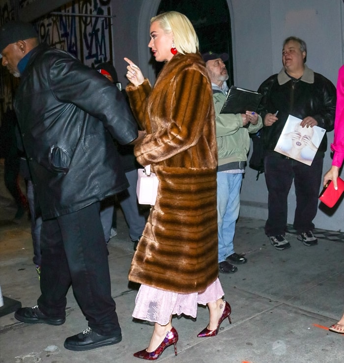 Katy Perry lets the lace hem of her Chika Kisada dress peek beneath her long faux-fur coat, finishing the Valentine’s Day look with pointed-toe stilettos from Katy Perry Collections
