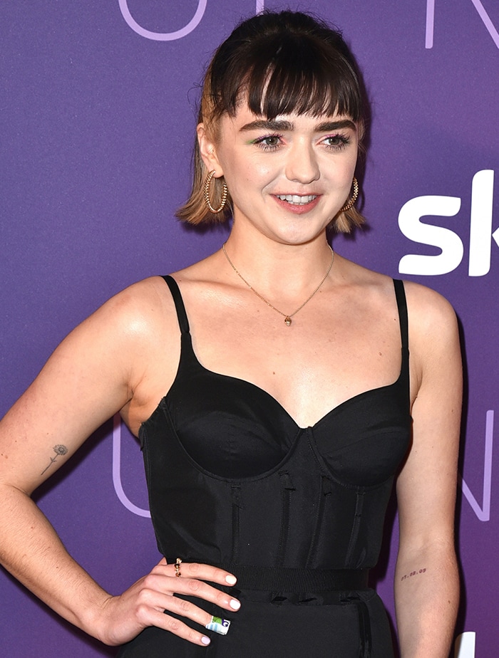 Maisie Williams completes her look with soft ombré hair, blunt bangs, and subtle gold jewelry that complements the structured elegance of her evening ensemble