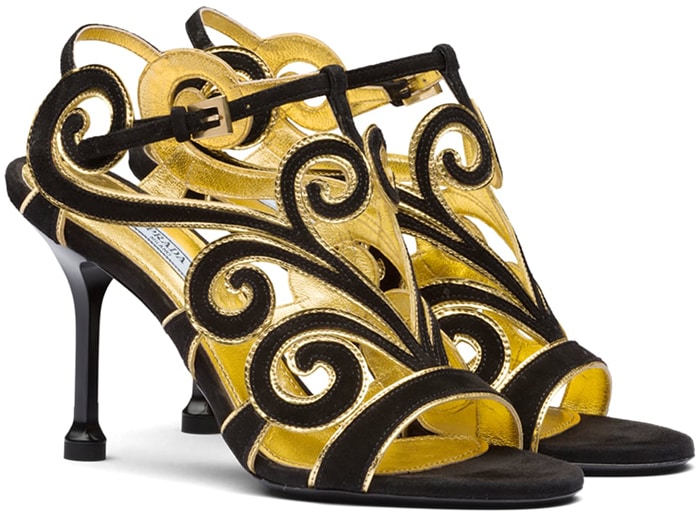Prada’s black suede sandals with curvy baroque gold-trimmed detailing feature an elegant open-toe silhouette set on a sculpted high heel and originally retailed for $950, reflecting the brand’s signature blend of craftsmanship and ornamental design