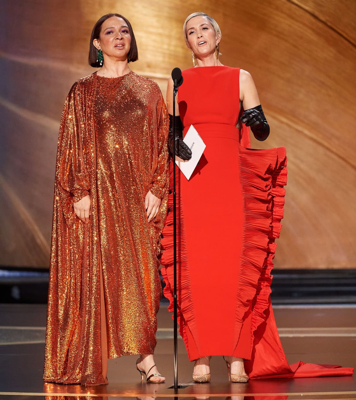 Presenting at the 92nd Academy Awards, Maya Rudolph anchored her copper sequined Valentino caftan with strappy metallic sandals, while Kristen Wiig paired her architectural red Valentino gown and black opera gloves with crystal-embellished gold Christian Louboutin "Maia Labella" pumps