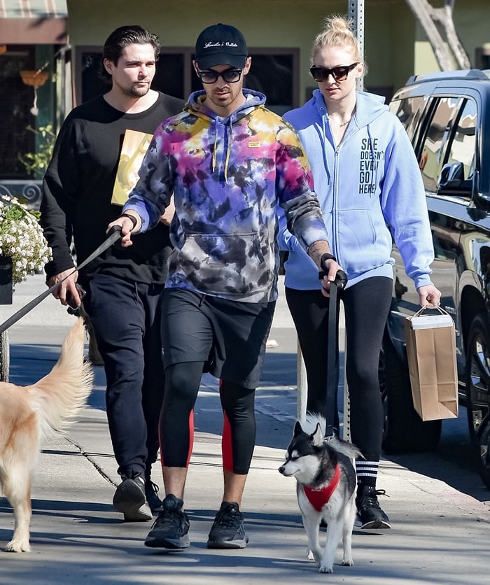 Sophie Turner pairs an oversized Mean Girls "She Doesn't Even Go Here" zip hoodie with black leggings, black crew socks, and white low-top sneakers