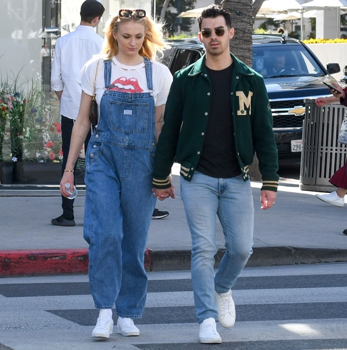 Sophie Turner styles Levi's Vintage "Dead Stone" denim overalls with a Rolling Stones graphic T-shirt and white Adidas Gazelle sneakers as she and Joe Jonas head out for smoothies