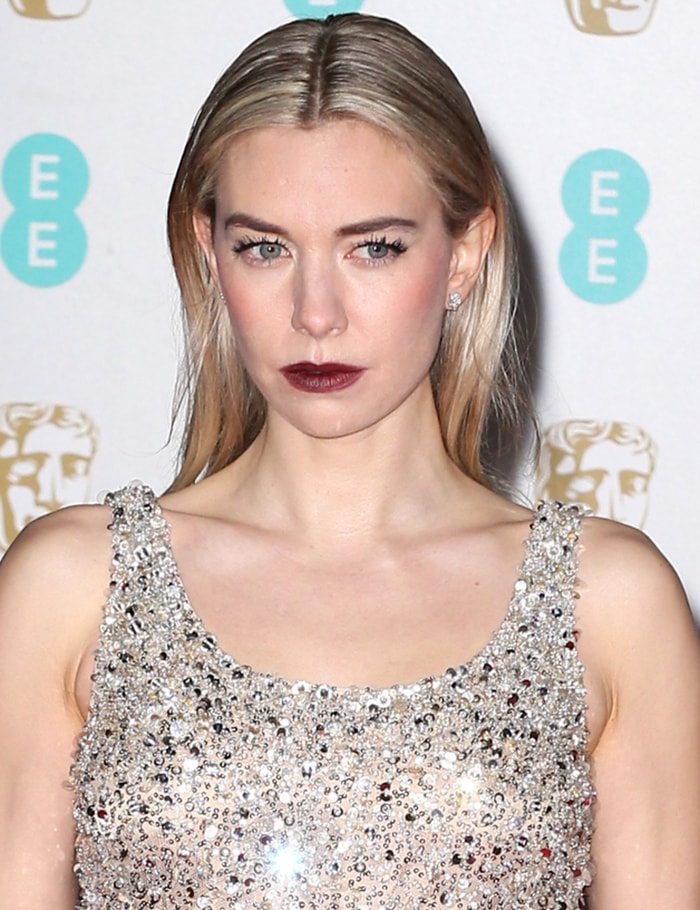 Vanessa Kirby contrasts her shimmering Valentino top with a sleek center-parted hairstyle and a bold wine-red lip for a striking BAFTA beauty moment