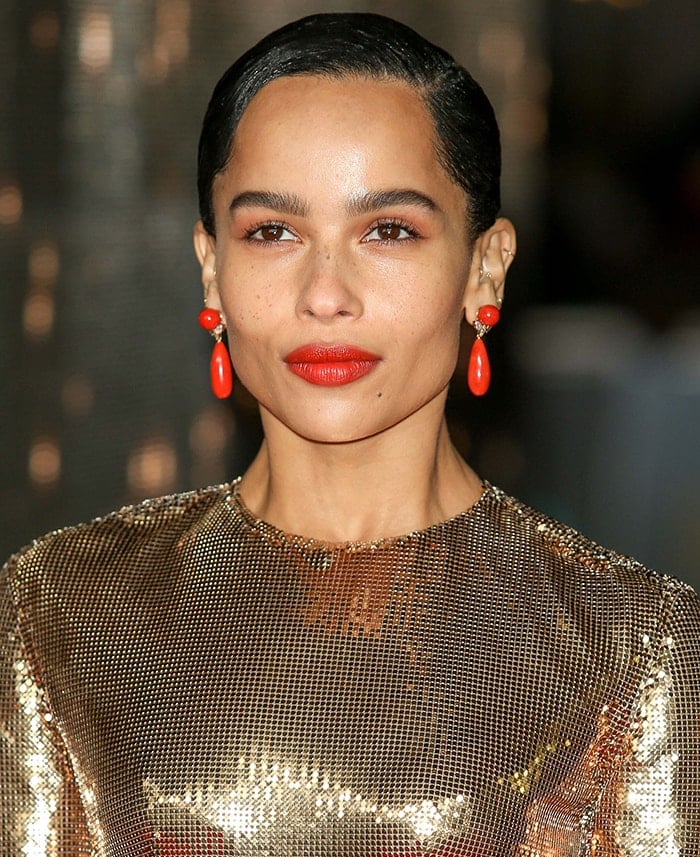 Zoë Kravitz pairs her liquid-gold Saint Laurent gown with a sleek, side-parted updo and bold red lips, punctuated by vibrant Assael Hearts Desire drop earrings