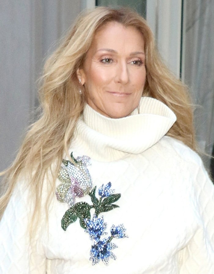 Celine Dion wears her hair in loose waves and keeps her makeup understated, allowing the embellished floral appliqué on her ivory Oscar de la Renta sweater to take center stage