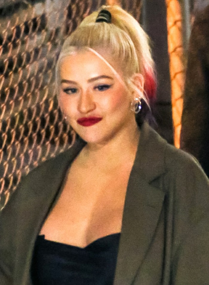 Christina Aguilera balanced dramatic red lipstick and a sleek high ponytail with minimal jewelry, letting the monochromatic styling carry the impact