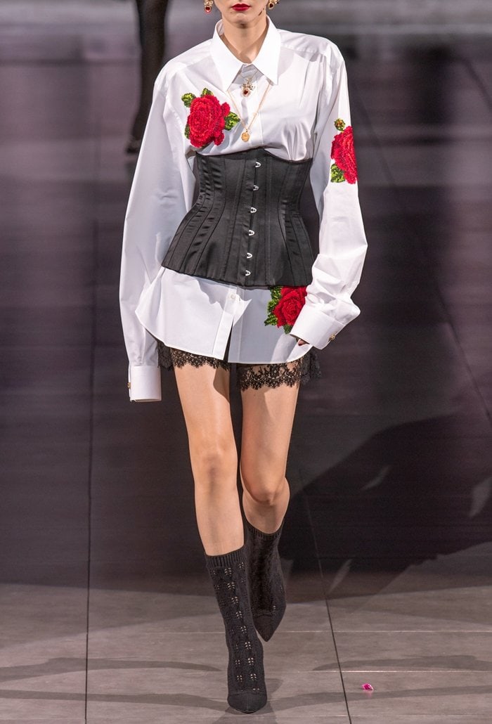 Dolce Gabbana Fall 2020 runway look featuring a white floral-embroidered shirt layered over lace-trimmed shorts and cinched with a structured black satin corset