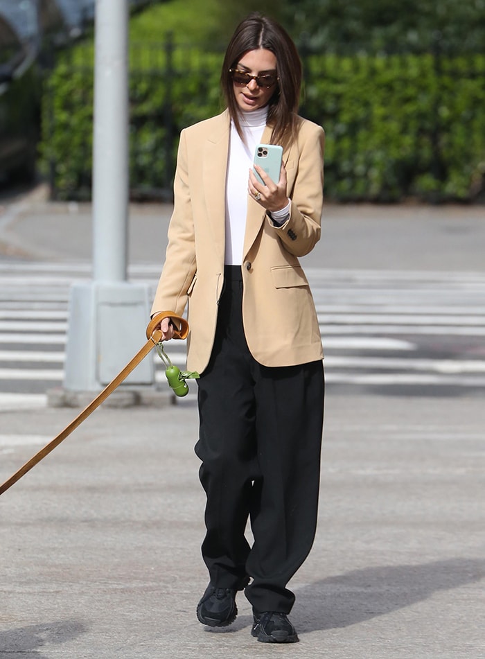 The oversized Givenchy blazer and slouchy trousers create a deliberately loose silhouette, while black sneakers keep Emily’s dog-walking look grounded and casual