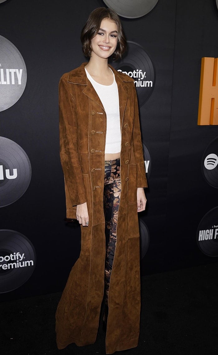 Kaia Gerber layers a white cropped tank and floral Charlotte Knowles trousers beneath a floor-length brown Fendi suede coat at the High Fidelity premiere in New York