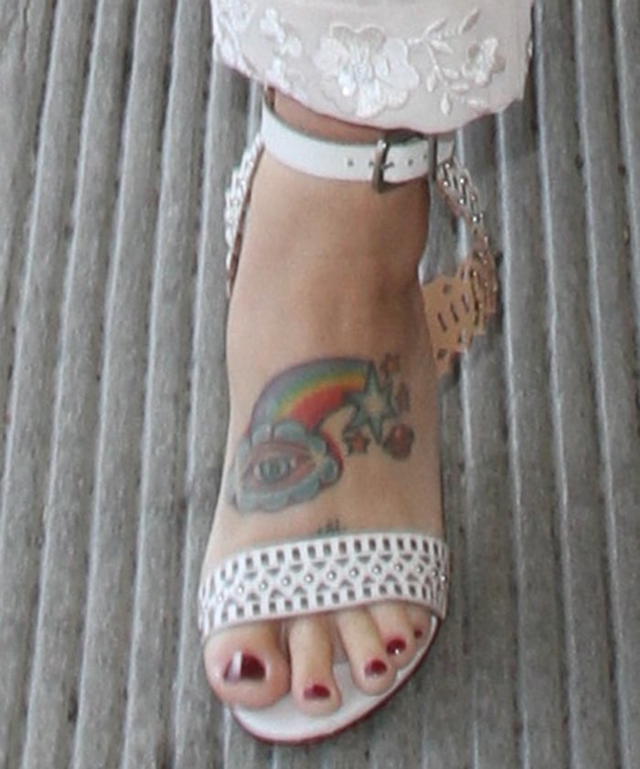 Kesha shows off her colorful foot tattoo featuring a rainbow, stars, and an eye while wearing white studded sandals, paired with a deep red pedicure