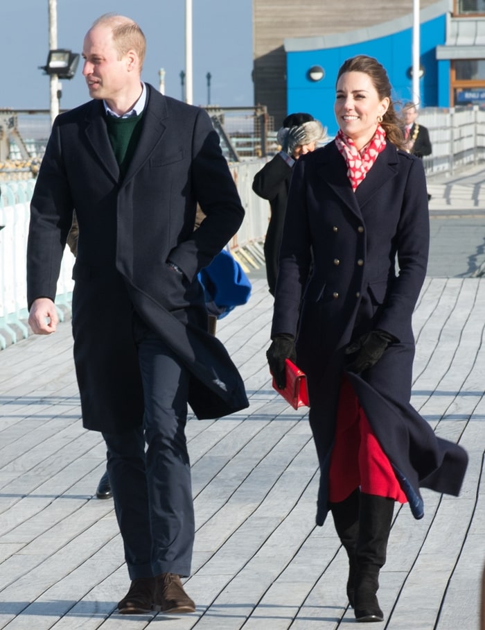 Kate layered a navy Hobbs coat over a vibrant red Zara dress, finishing the look with a matching Mulberry clutch and knee-high suede boots for the windswept visit to Swansea