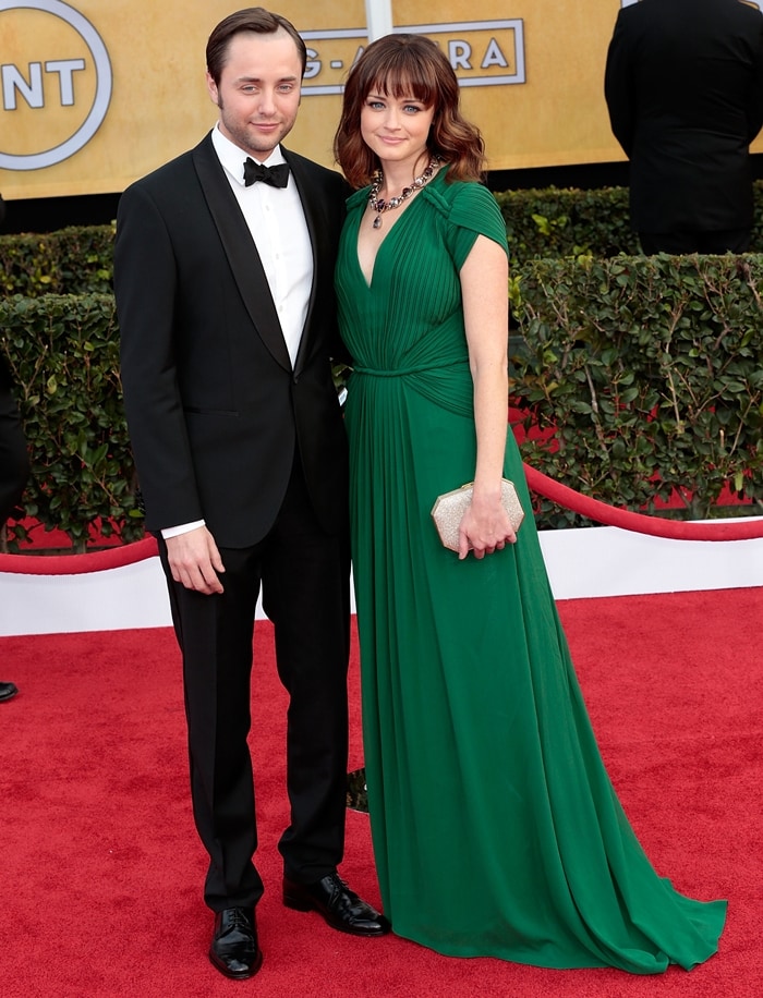 Vincent Kartheiser and Alexis Bledel exude classic elegance on the red carpet, with Alexis stunning in an emerald green gown featuring delicate pleating and a deep V-neckline, perfectly complemented by a sparkling clutch and statement necklace