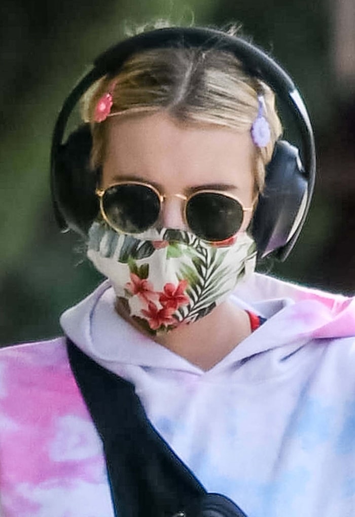 Emma Roberts wearing a floral face mask, Ray-Ban sunglasses, flower snap clips, and a tie-dye hoodie