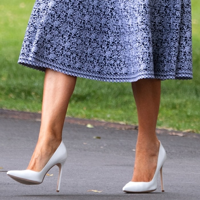 Melania Trump grounds the look with white Manolo Blahnik “BB” pumps, their sharp pointed toe and slim stiletto extending the line beneath her blue lace midi skirt while keeping the finish clean and controlled