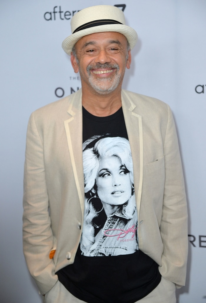 Christian Louboutin attends an event in a casual cream blazer, straw hat, and a Dolly Parton graphic tee — a reminder that his French surname is pronounced “Loo-boo-tan”