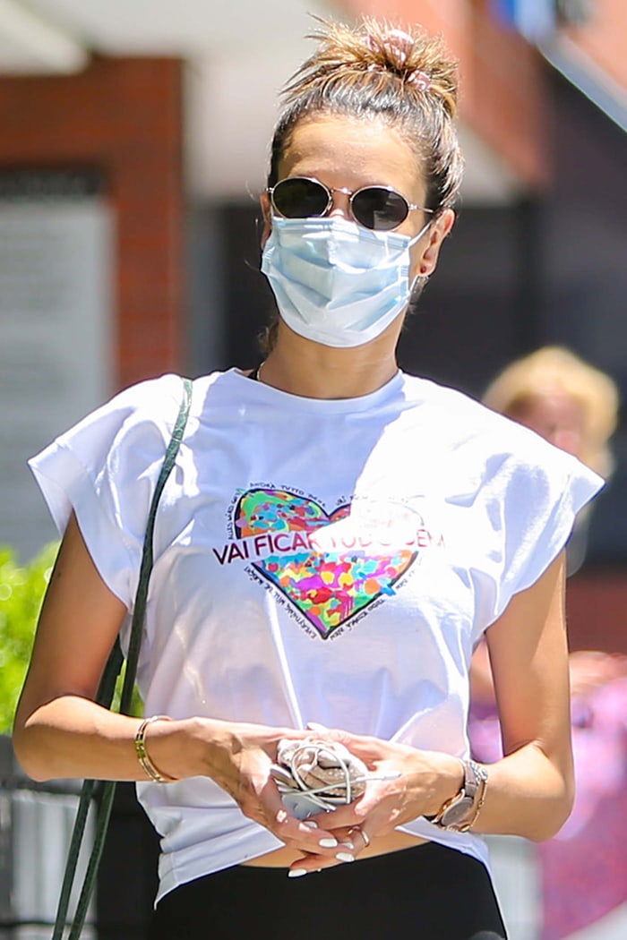 Alessandra Ambrosio wearing round sunglasses, a white face mask, and her hair in a topknot