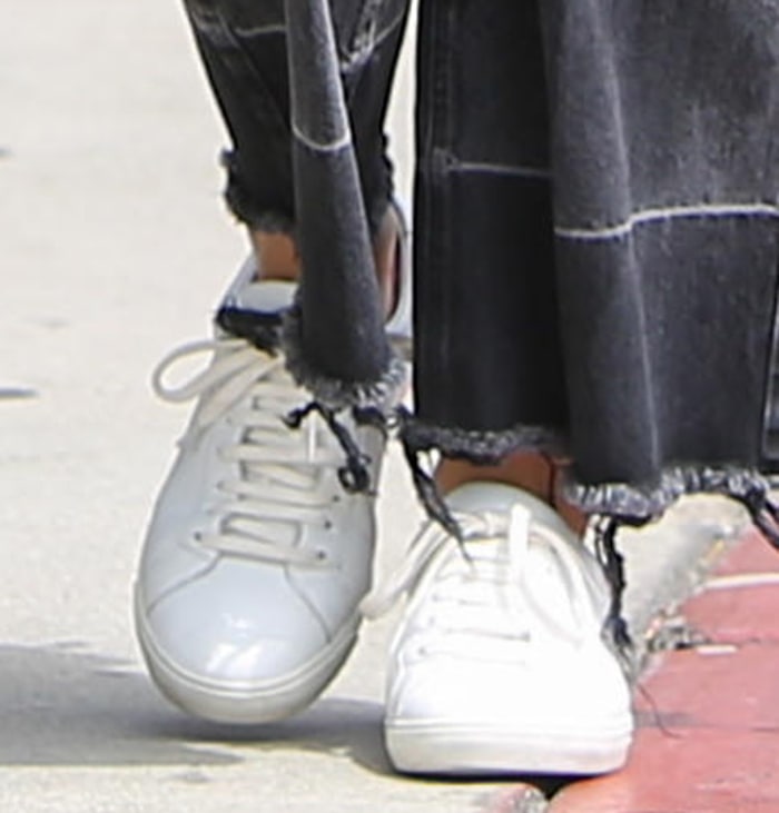 Ana de Armas grounds her relaxed lunch-date look with white Saint Laurent “Andy” leather sneakers, pairing the minimalist low-tops with frayed-hem Rachel Comey denim for an effortless blend of comfort and understated luxury