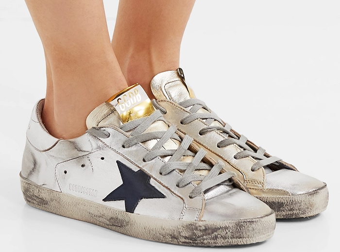 The iconic Golden Goose Super-Star sneaker features premium metallic leather accents, gray flat laces, and a pre-scuffed vintage aesthetic
