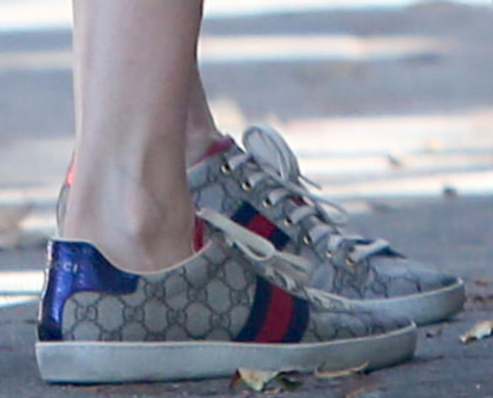Laura Dern’s Gucci New Ace sneakers combine the house’s signature GG Supreme monogram canvas with classic red-and-blue Web stripes and contrasting metallic heel tabs for a polished take on everyday streetwear