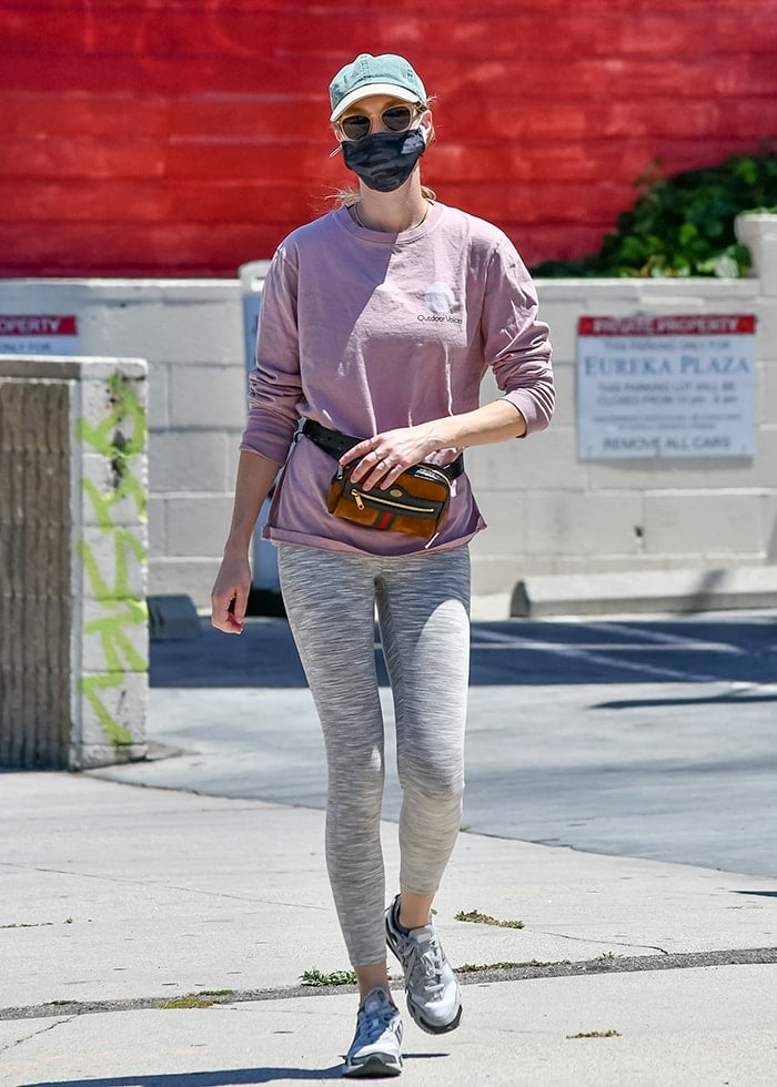 Whitney Port pairs gray cropped leggings with a dusty rose Outdoor Voices sweatshirt and gray New Balance running shoes, accessorizing with a Gucci Ophidia GG suede belt bag, baseball cap, sunglasses, and black face mask