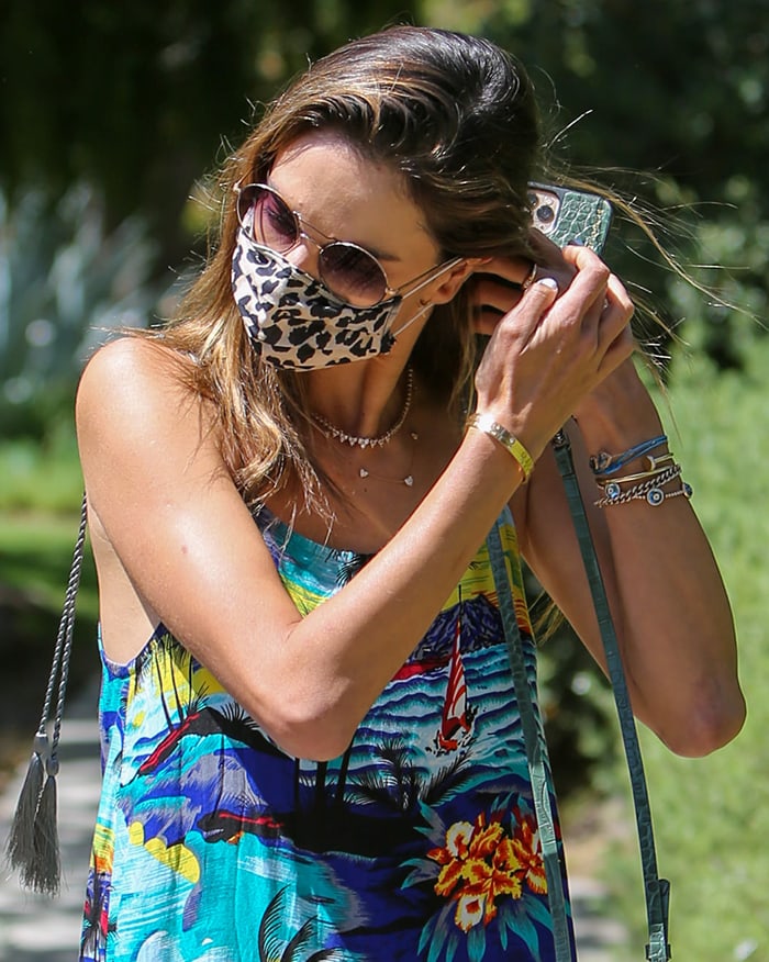 Alessandra Ambrosio wears sunglasses, layered jewelry, and a leopard-print face mask