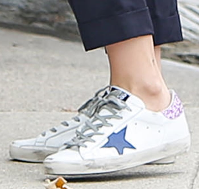 Ana de Armas’ Golden Goose Superstar sneakers feature distressed white leather, blue star patches, gray laces, and lilac glitter heel tabs