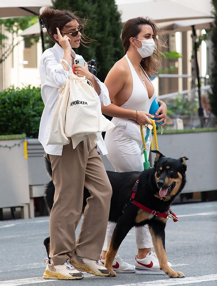 Emily Ratajkowski walks her dog Colombo in NYC on July 28, 2020, styling relaxed khaki trousers with Travis Scott x Nike Air Max 270 “Cactus Trails” sneakers, whose chunky, trail-inspired sole grounds her oversized white shirt and off-duty summer layers