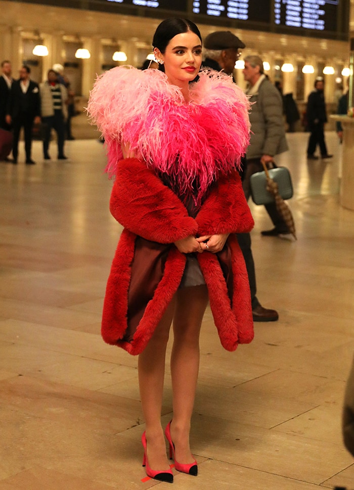 Lucy Hale filming Katy Keene at Grand Central Terminal in New York City on February 7, 2020, wearing black-and-pink Saint Laurent “Anja” pumps with a dramatic feathered neckline and oversized red coat that captured the series’ bold, fashion-driven styling