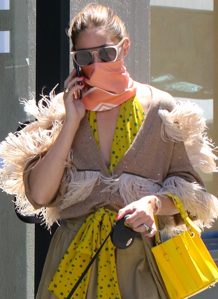 A close-up reveals how oversized sunglasses, a silk scarf face covering, feather trims, and a Piaget watch combine into one of her most memorable street-style looks