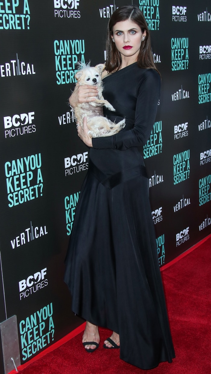 Alexandra Daddario radiates elegance in an all-black ensemble while holding her adorable dog at the Can You Keep a Secret? premiere, pairing a sleek black top and flowing skirt with strappy sandals for a chic red carpet look