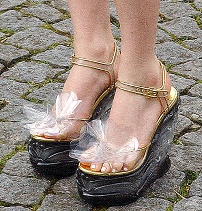 Maisie Williams added some height in whimsical platform sandals featuring clear tulle bows, gold straps, and chunky sculptural soles that framed her petite feet