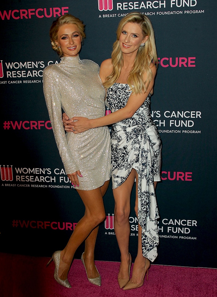 Nicky Hilton stuns in nude pointed-toe pumps paired with a sophisticated monochrome gown, while Paris Hilton sparkles in metallic heels and a shimmering mini dress at the An Unforgettable Evening event on February 27, 2020