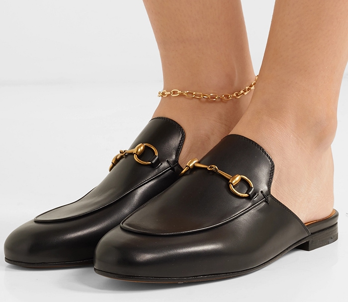 Black leather Gucci Princetown slippers feature gold horsebit hardware, an open back, and a low heel