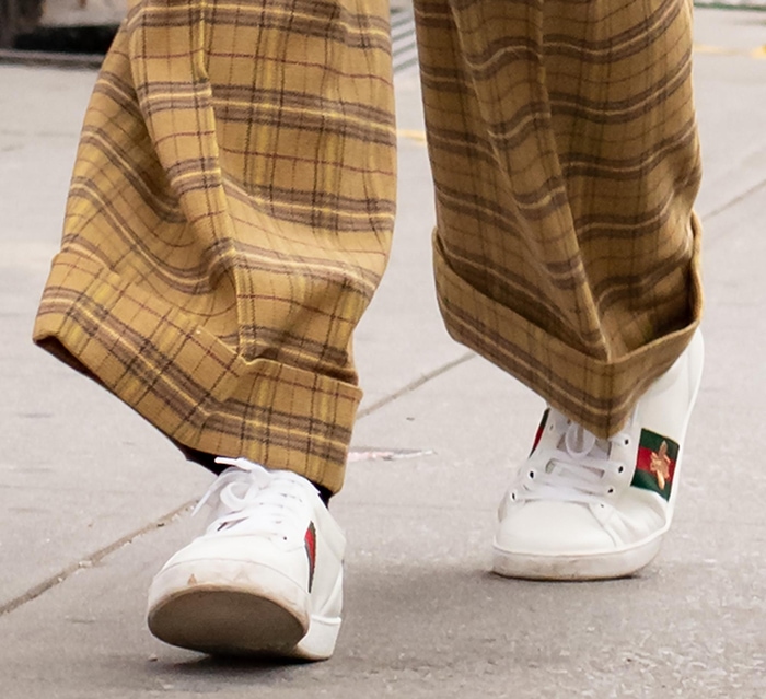 Katie Holmes grounds her ’90s-inspired plaid trousers with white Gucci New Ace sneakers, where signature Web stripes and gold bee embroidery add a polished, heritage finish to the relaxed silhouette