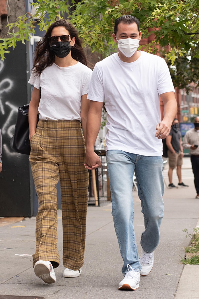 Katie Holmes and Emilio Vitolo Jr. step out in coordinated white tees and face masks, with Holmes grounding her ’90s-inspired plaid trousers in classic Gucci sneakers as the pair walk hand in hand through SoHo